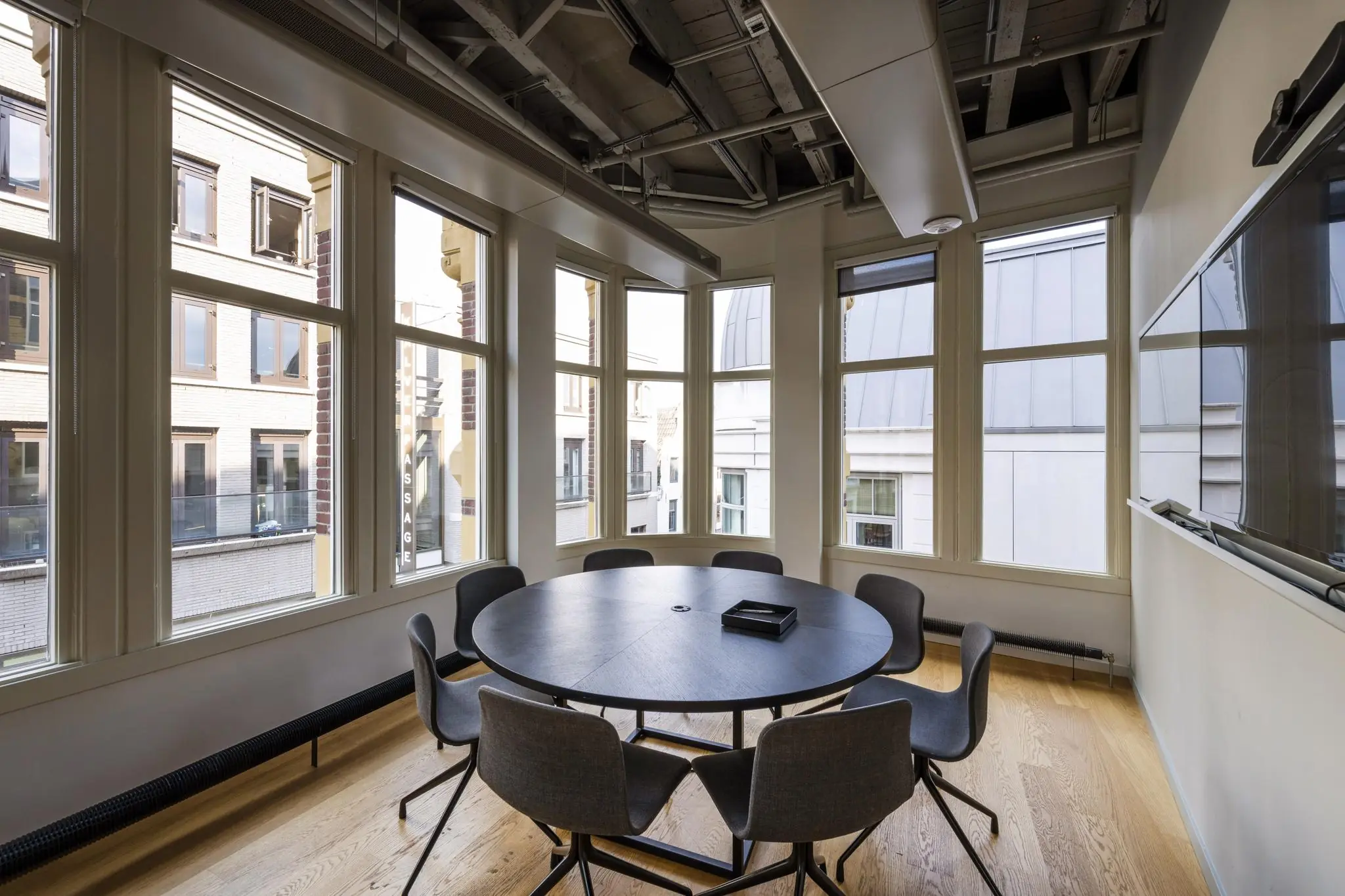 Vergaderruimte met ronde tafel en zes stoelen, omringd door grote ramen in een pand aan de Sint-Jorissteeg.